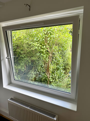 Large white replacement window giving a clear garden view from an Altrincham home
