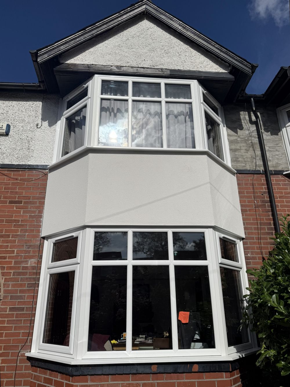 Front view of the completed bay rebuild with white windows and new rendering between floors.